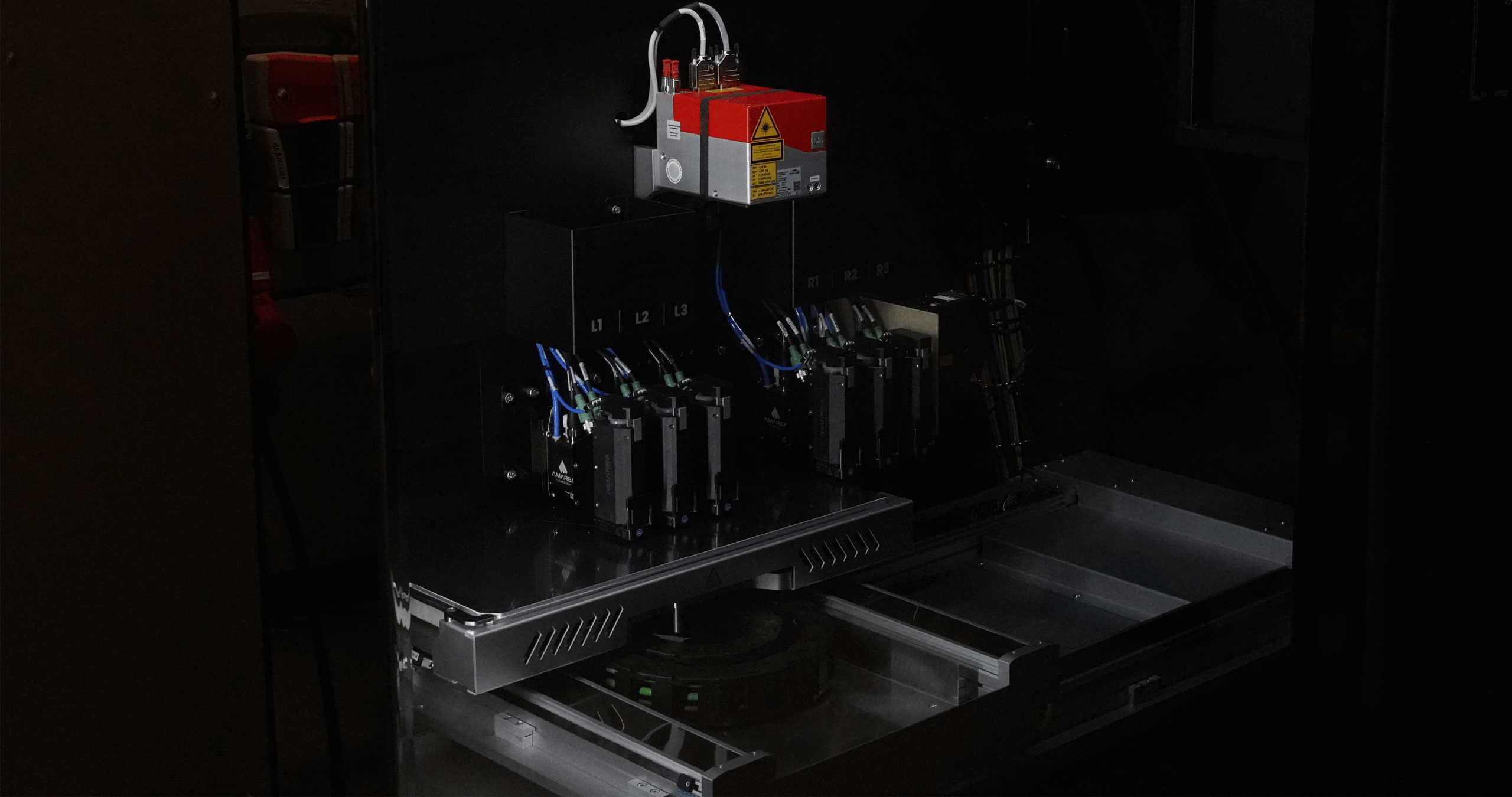 Build chamber view showing six print heads and laser optics of the subtractive module.